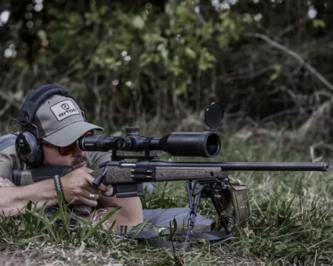 Long range shooter aiming a rifle with a scope in the grass