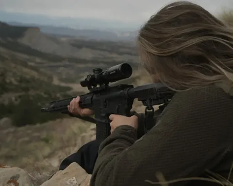 woman holding an AR with an LPVO optic while aiming down a hill