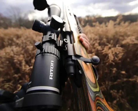 Someone holding a hunting rifle with a scope in a prairie