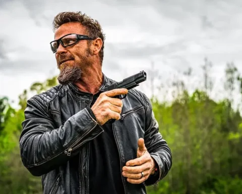 man wearing a leather jacket holding a pistol