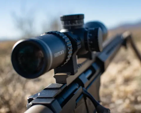 rifle with a view of the ocular side of a scope in tall grass