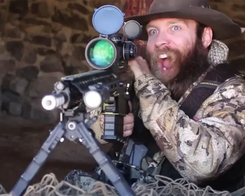 man with an excited look holding a long range rifle out a window